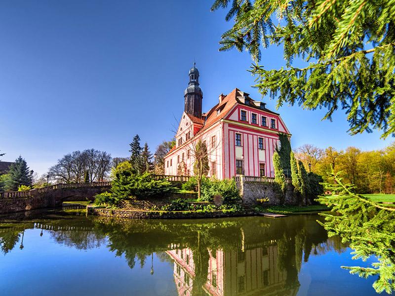 Schloss spiegelt sich im Graben zwischen frischem Grün