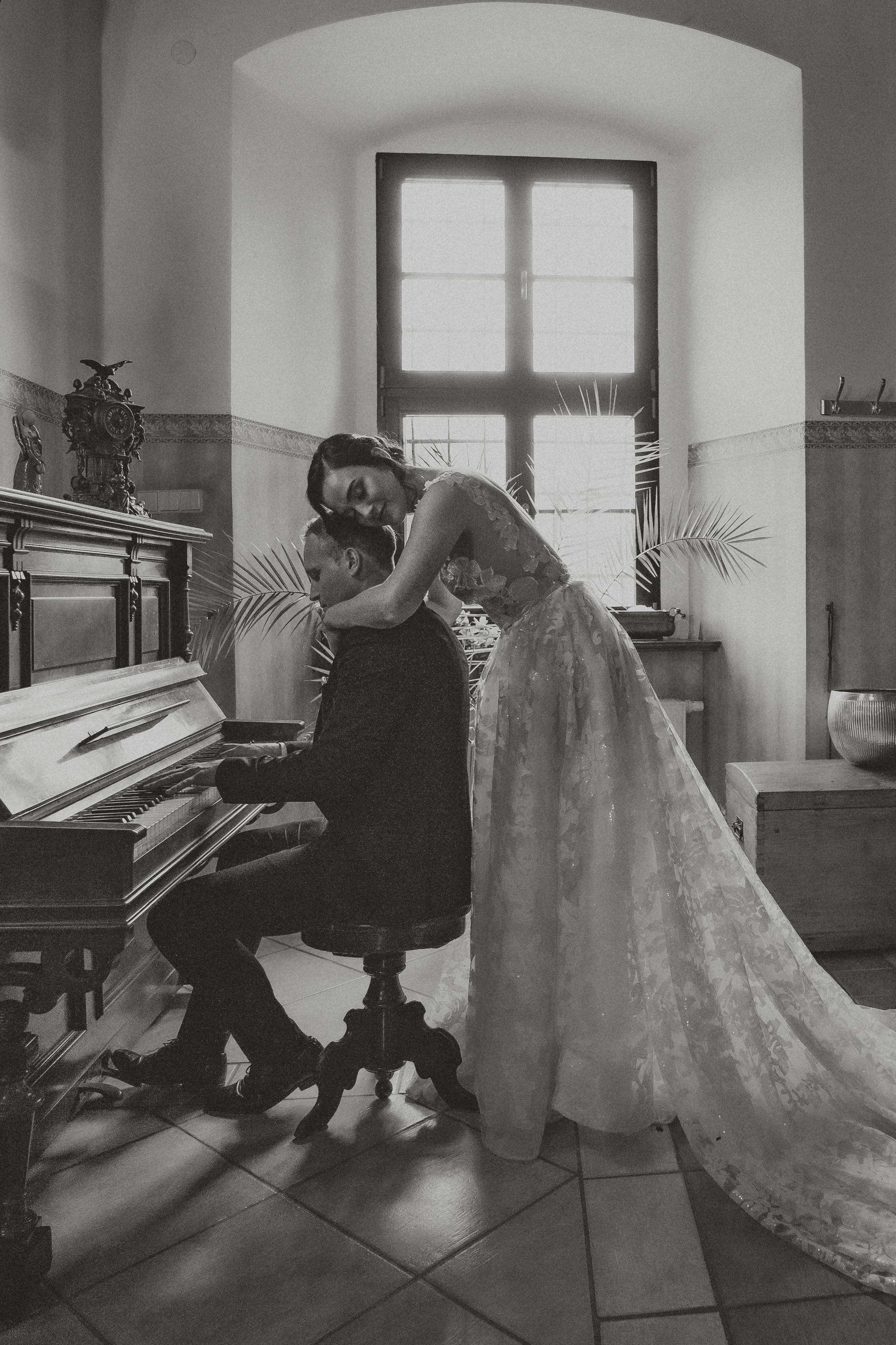 Schwarzweißfoto eines Brautpaars am Klavier im Schlossfenster