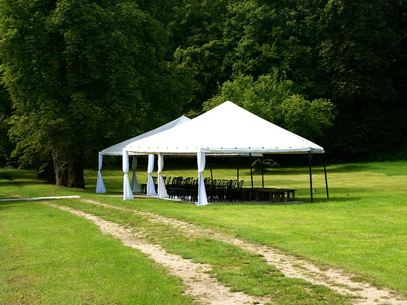 Marquee with laid tables on a green clearing by the forest