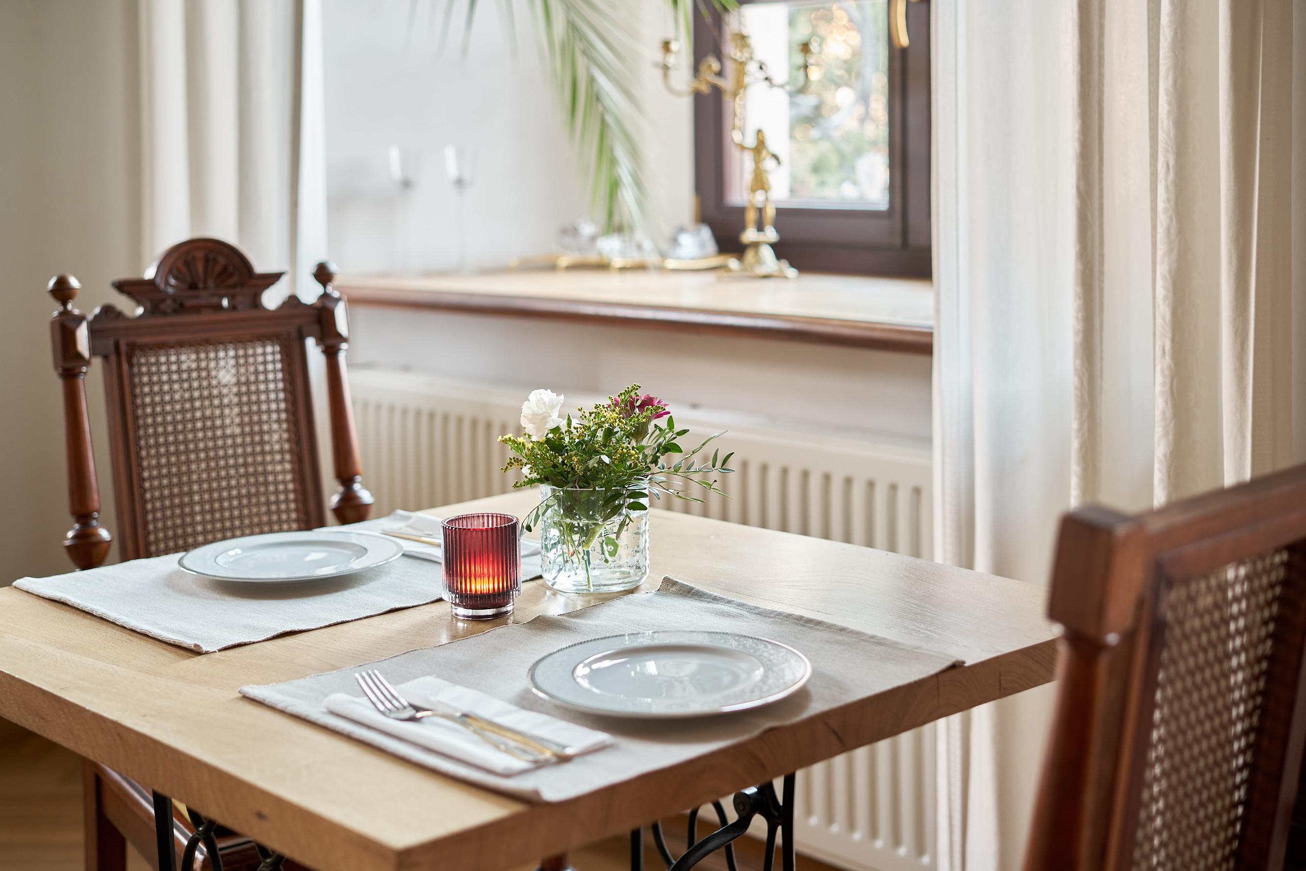 A laid table with flowers and a candle by the window