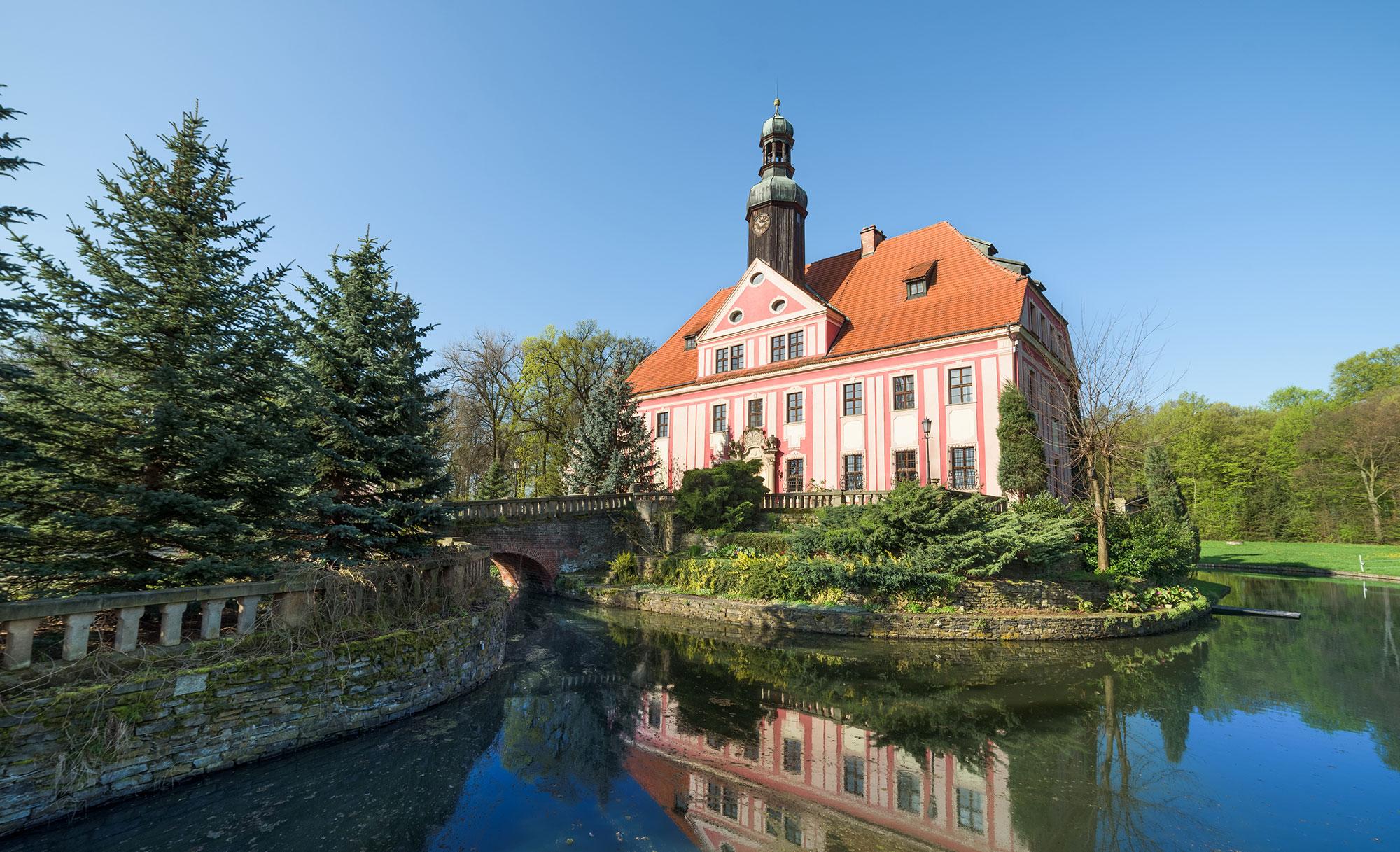 The palace surrounded by its moat, a stone bridge and spruces in the park